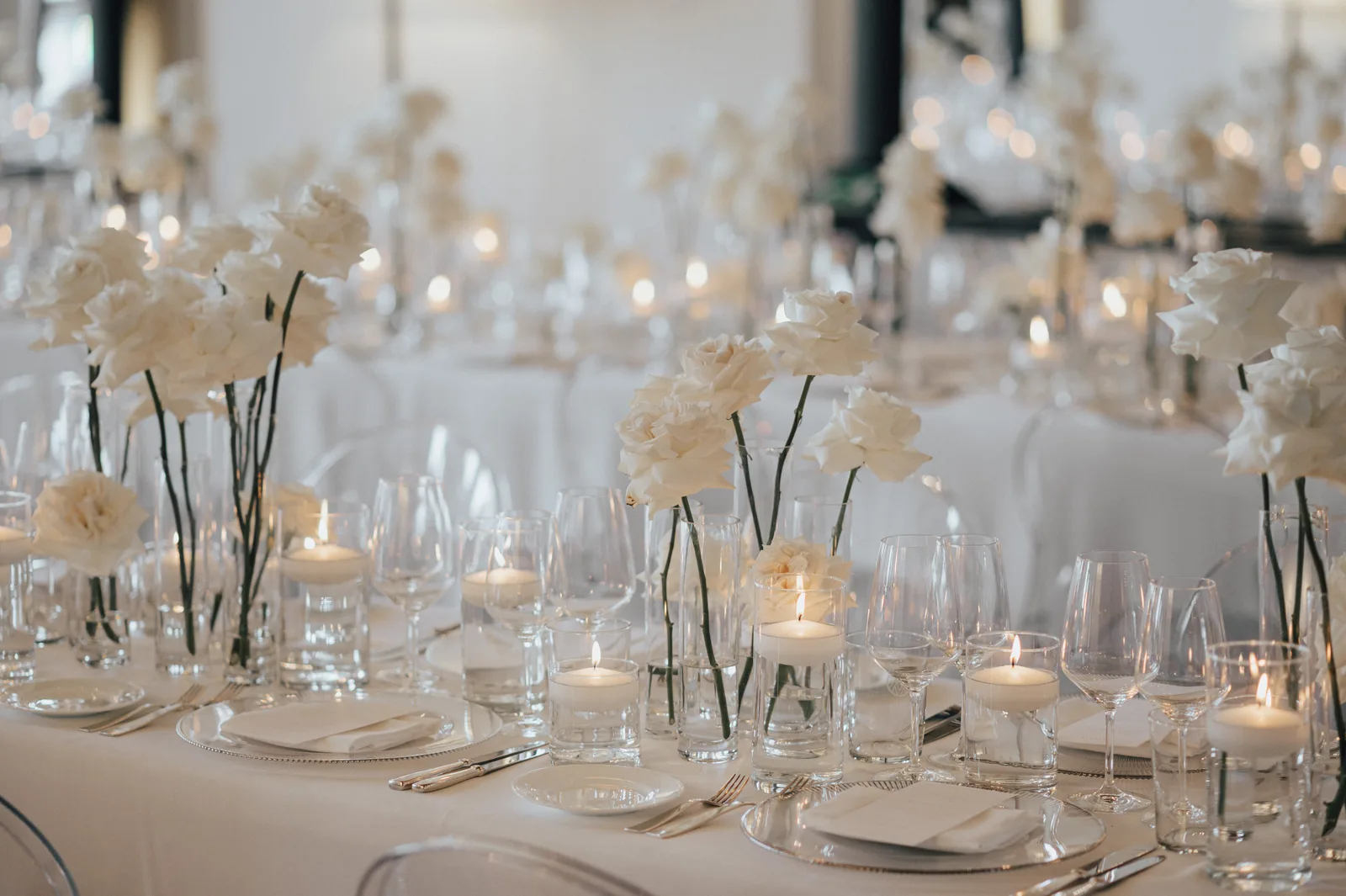 Hochzeitstafel mit weißen Rosen, Kerzen und Glasvasen